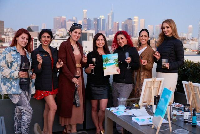 Group of women celebrating after a Paint and Sip event with the Los Angeles skyline behind them