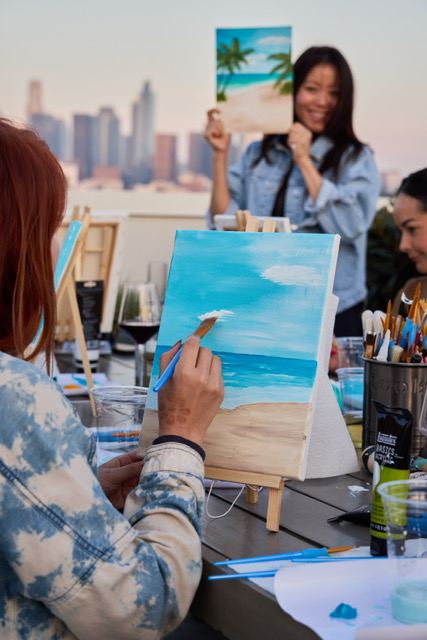 Guests painting their canvases during a Wellness Atelier Paint and Sip event with wine and art supplies