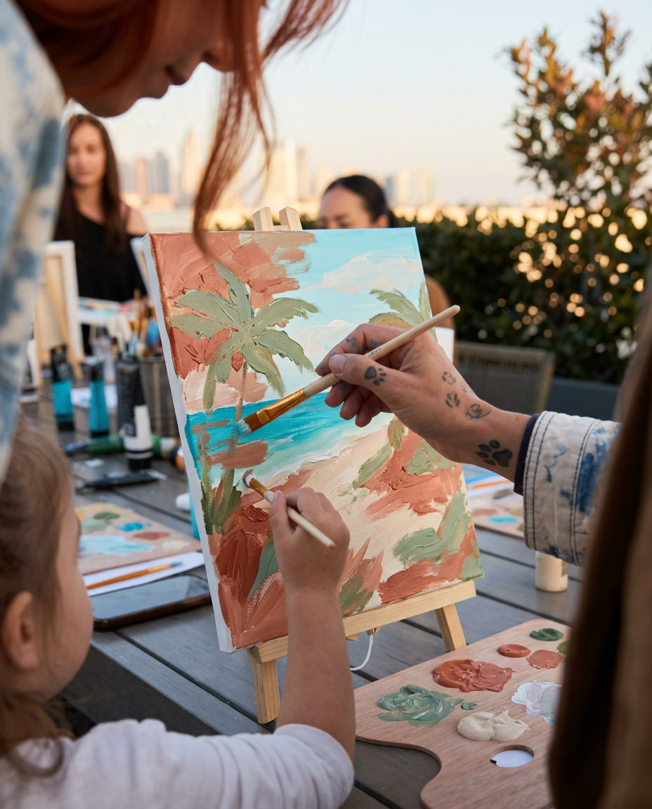 Close-up of a child and mother painting a beach scene together on the same canvas at a Wellness Atelier family paint class